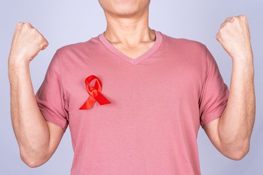 Red AIDS awareness ribbon on man chest and raise his hand to fight them on grey background. World Aids Day, Healthcare and medical concept.