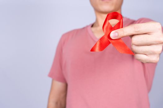Red AIDS awareness ribbon holding by man on grey background. World Aids Day, Healthcare and medical concept.