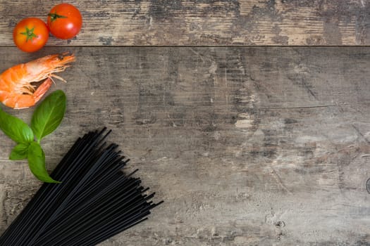 Raw black spaghetti with prawns, tomatoes and basil on wooden background