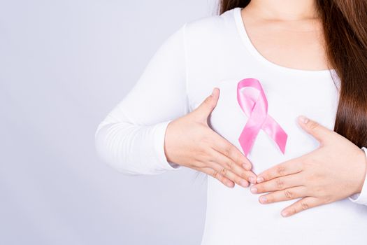 Breast cancer awareness ribbon on woman chest and doing self exam on grey background. Medical, healthcare for advertising concept.