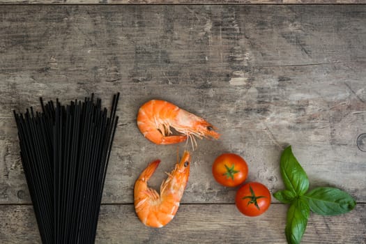 Raw black spaghetti with prawns, tomatoes and basil on wooden background