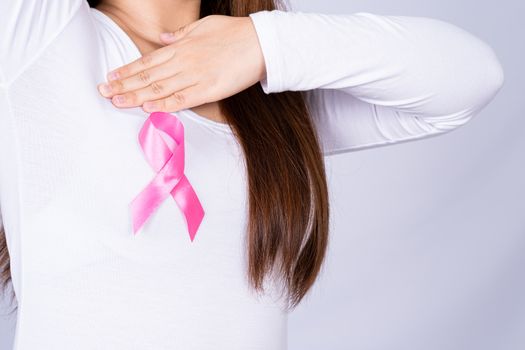 Breast cancer awareness ribbon on woman chest and doing self exam on grey background. Medical, healthcare for advertising concept.