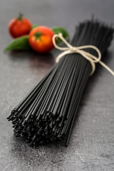 Black spaghetti, basil and tomatoes on black slate background