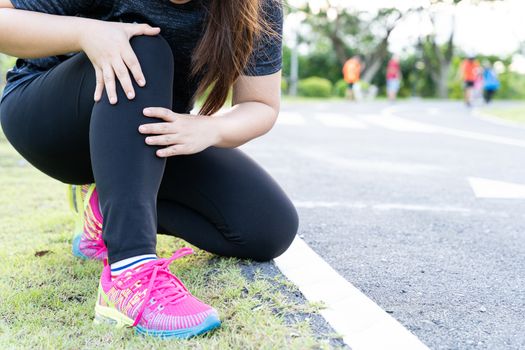 Asian woman use hands hold on her knee injury while running on road in the park, Injury from workout concept.