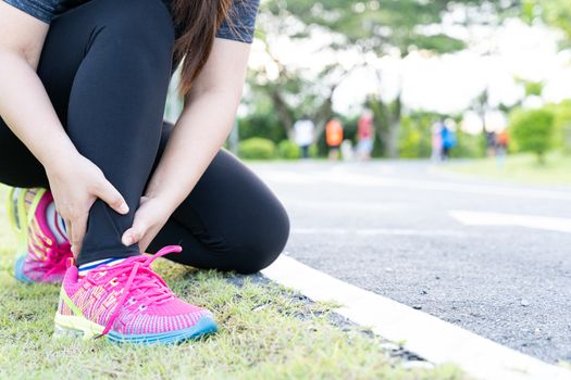 Asian woman use hands hold on her ankle while running on road in the park. Injury from workout concept.