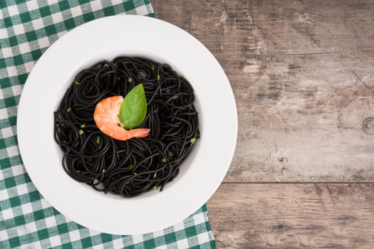 Black spaghetti with prawns and basil on wooden table