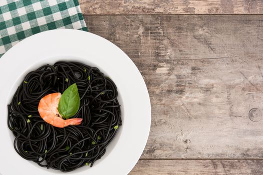 Black spaghetti with prawns and basil on wooden table