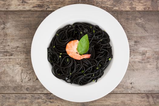 Black spaghetti with prawns and basil on wooden table