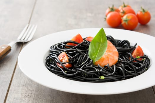 Black spaghetti with prawns and basil on wooden table