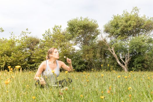Woman in sportswear sitting in the park blowing a dandelion