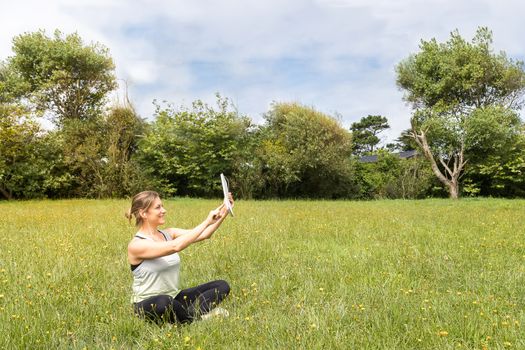 Woman in sportswear taking a self-portrait with a tablet sitting in the park