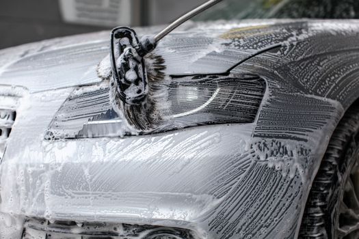 Detail on car front light being washed with soap foam in car wash.