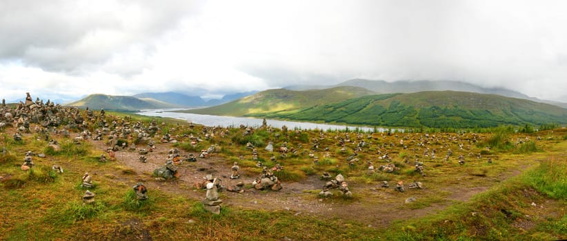 Small piles of stones made by tourists on viewpoint overlooking one of many scottish lochs in highlands.