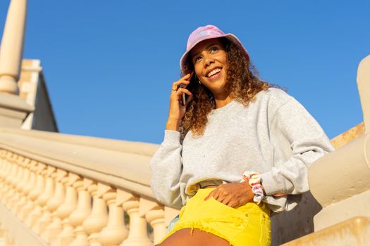 Portrait of an attractive young black woman sitting and talking with the mobile phone outdoors with her mask off. Concept communication