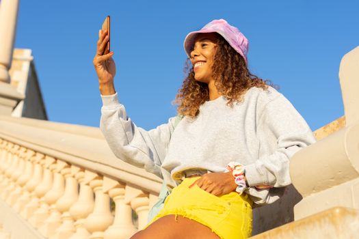 Portrait of an attractive young black woman sitting and talking with the mobile phone outdoors with her mask off. Concept communication