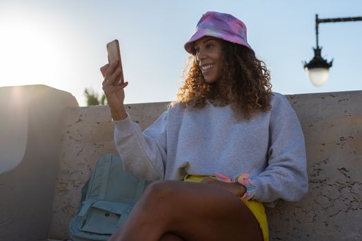 Portrait of an attractive young black woman sitting and talking with the mobile phone outdoors with her mask off. Concept communication