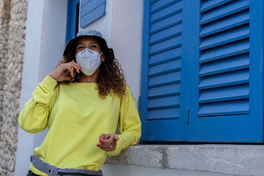 Portrait of an attractive young black woman sitting and talking with the mobile phone outdoors with her mask off. Concept communication
