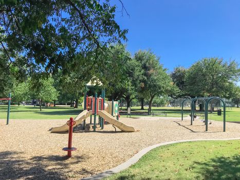 Large tree shade and colorful urban playground at public park in downtown Dallas, Texas, America. Empty recreation place in hot summer day with sunny clear blue sky.