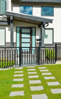 Entrance of new residential house with concrete tile pathway over front yard and metal fence in front