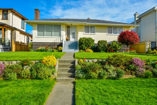 Average family residential house with landscaped front yard on blue sky background