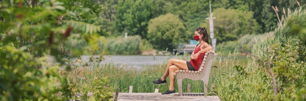 Mask wearing woman sitting relaxing on bench outside in summer nature park for coronavirus prevention. Protectve face covering COVID-19 lifestyle. Banner panoramic.