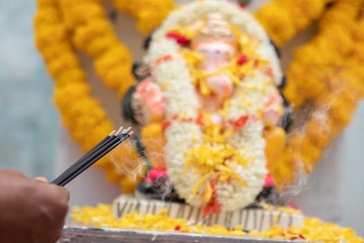 Hands Holding or offering incense or agarbatti stick in front of lord vinayaka or Ganesha while praying or worshiping during festival ceremony.