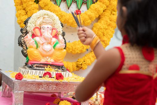 kid praying by closing eyes infront of god Ganesha idol by holding or offering incense in hand during ganapati festival celebration at home