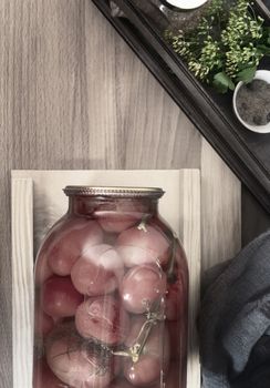 Home preservation: a large glass jar with red ripe pickled tomatoes, closed with a metal lid, next to spices and herbs. Top view, close-up.