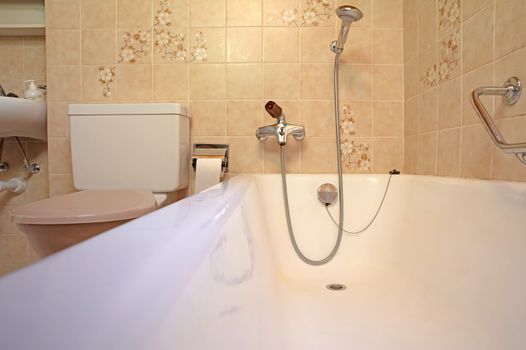 Old bathroom, brown tiled interior with bathtub, assistive handle