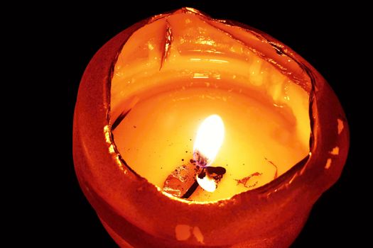 A closeup of an illuminated orange burning candle in dark.