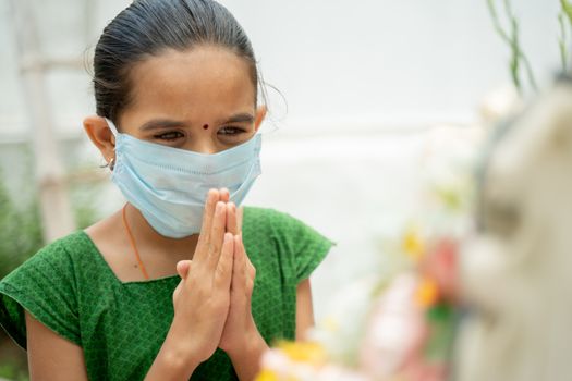 Young girl kid in medical mask praying to god to protect from coronavirus or covid-19 by folding hands in namaste gesture