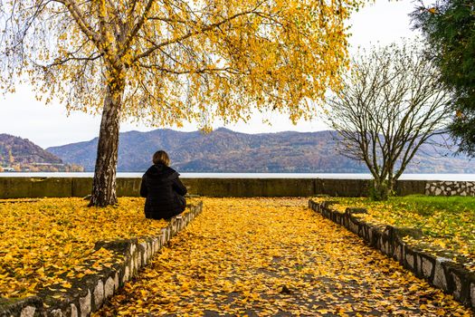 Autumn leaves fallen on standing alone woman on the autumn alley. Autumn landscape, orange foliage in a park in Orsova, Romania, 2020