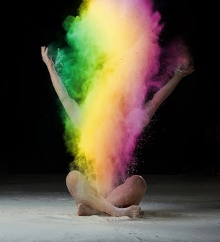 caucasian woman sits on the floor and throws colored powder up, black background