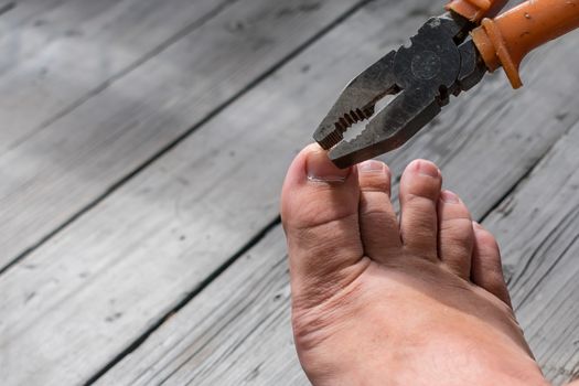 A man during work cuts his toenails in an unusual way with the help of working pliers