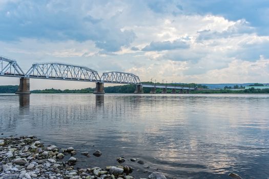 View from the rocky bank to the railway bridge over the river in cloudy weather