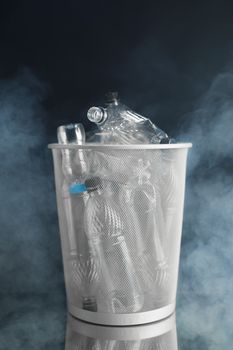 trash can with wasted plastic bottles, black background with smoke, pollution concept