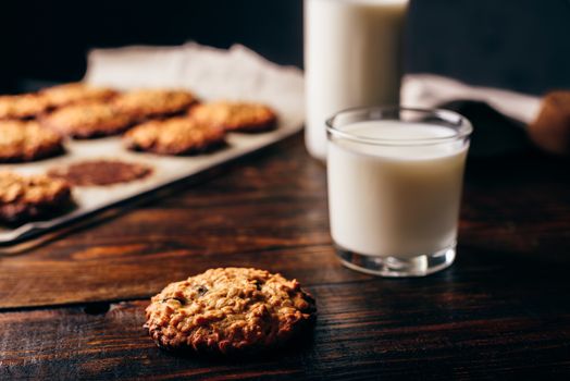 Homemade Oatmeal Cookies with Raisins and Glass of Milk for Breakfast. Some Cookies on Parchment Paper with Bottle on Backdrop.