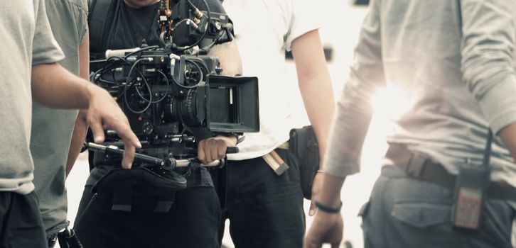 Blurred images of high definition video camera and lens on steady equipment support such as gimbal steady or stabilized shoulder rig and pan tilt shift head tripod for handheld filming a fast moving object in tv commercial production at outdoor location.