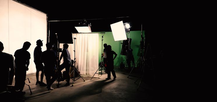 Behind the scenes of TV commercial movie film or video shooting production which crew team and camera man setting up green screen for chroma key technique in big studio.