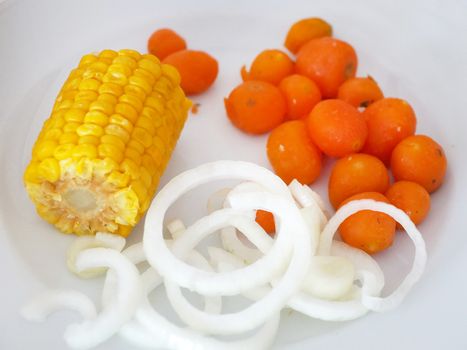 boiled corn, carrots and onions in rings on a white plate