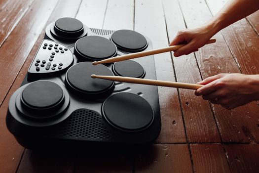 hands playing on portable electronic drums, brown background