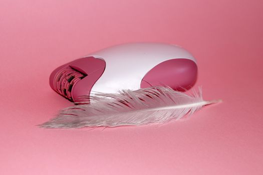 electric handheld epilator and feather on pink background close-up