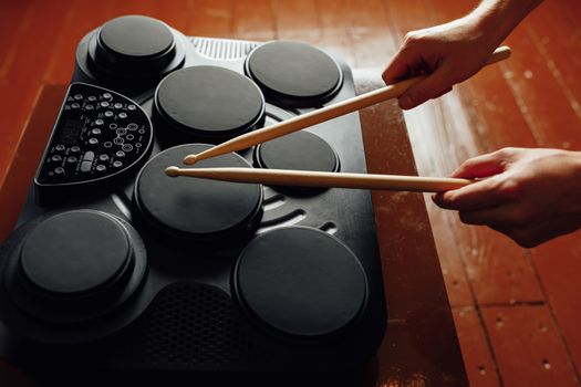 hands playing on portable electronic drums, brown background