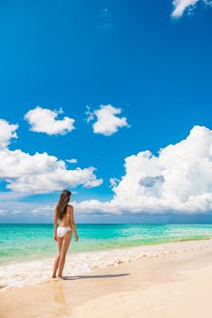 Beach vacation travel luxury swimsuit woman relaxing on summer holidays with copy space ocean, white sand and blue sky paradise landscape background.