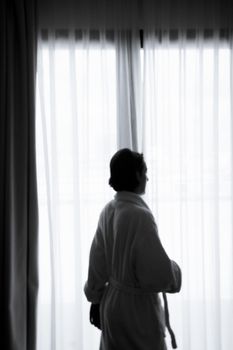 Silhouette of woman with bathrobe in front of a window. Sad atmosphere