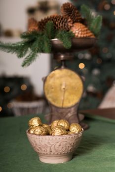 A basket of sweets wrapped in foil, on the table next to the tea set. green Christmas tree with bumps on defocus background. Comfort in home.