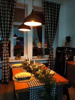 The festive Christmas kitchen table is decorated with branches of a Christmas tree, candles and garlands. Cozy home Christmas atmosphere