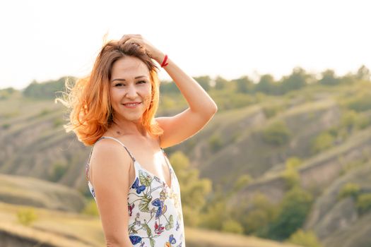 Tender beautiful red-haired girl enjoys the sunset in a field with a hill