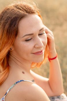 Tender beautiful red-haired girl enjoys the sunset in a field with a hill