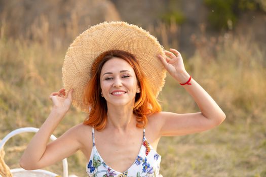 Beautiful red-haired girl enjoys the sunset on the nature. Picnic in the field